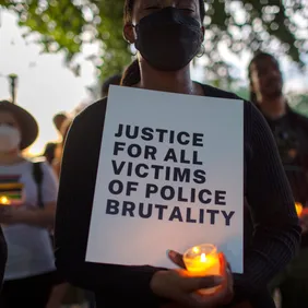 A demonstrator holding a candle and a sign with Justice For