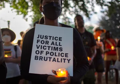 A demonstrator holding a candle and a sign with Justice For